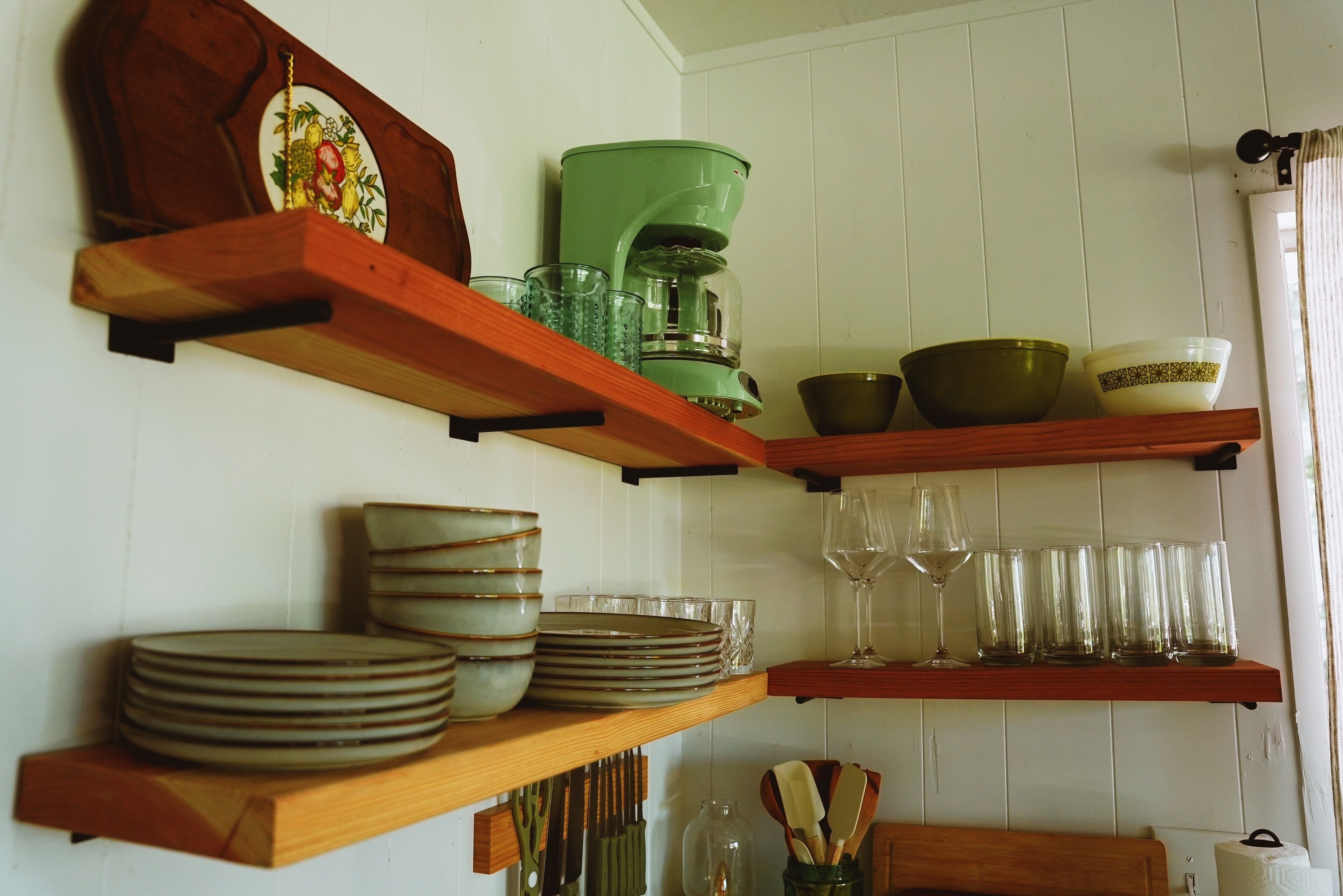 Una cocina con estantes de madera que contienen platos, tazones, vasos y una cafetera.