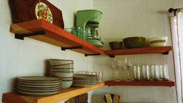 Una cocina con estantes de madera que contienen platos, tazones, vasos y una cafetera.
