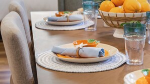 Una mesa de comedor con platos, vasos y una cesta de naranjas.