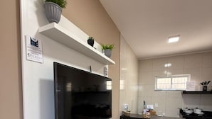 Una cocina moderna con televisión de pantalla plana, armarios blancos, una ventana y estufa a gas.