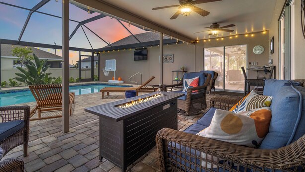 Un patio exterior con piscina, muebles de mimbre, ventiladores de techo y luces colgantes.