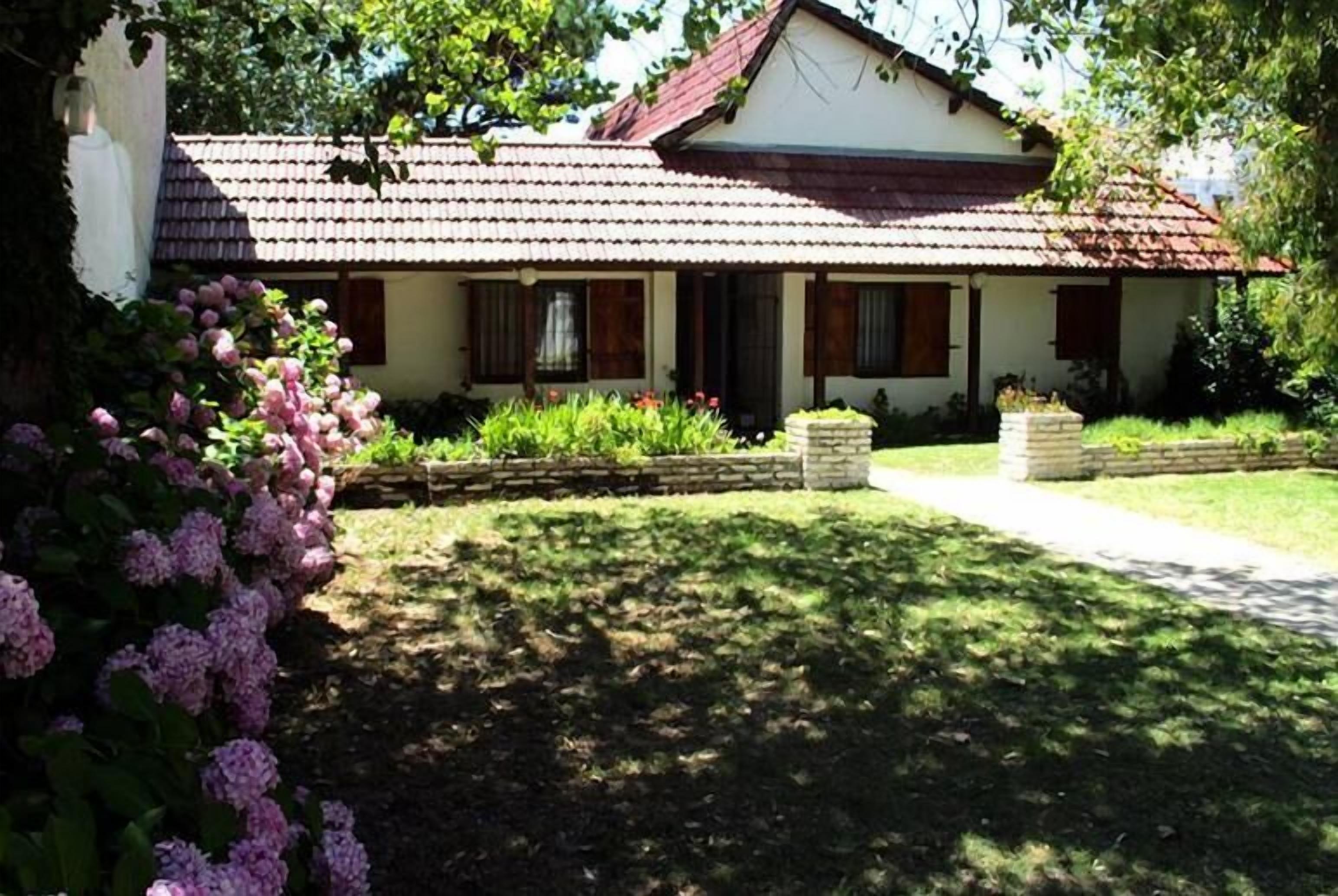 Una casa de un piso con tejado de tejas, un porche delantero y un jardín bien cuidado con flores rosas.