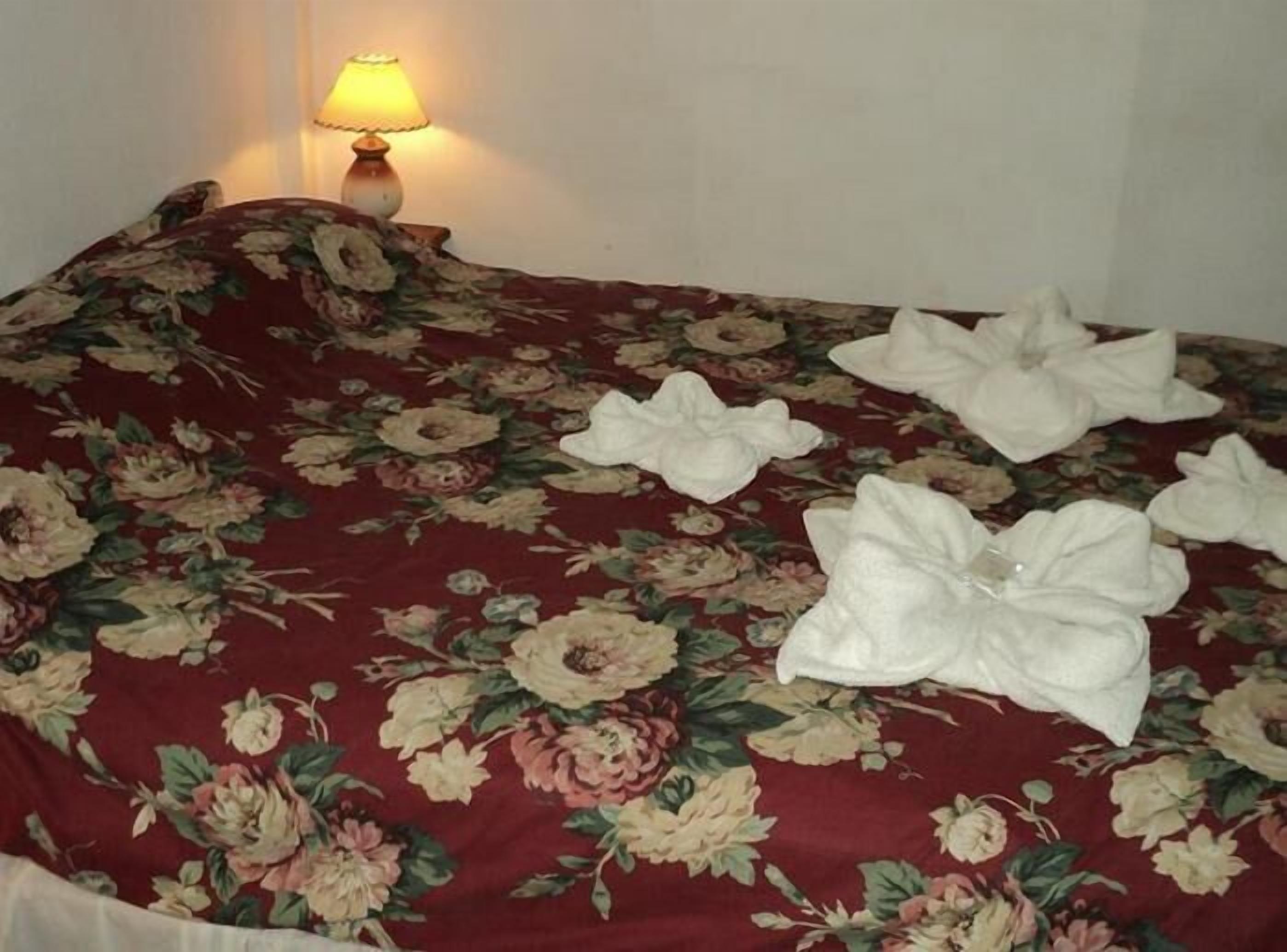 Una cama con un edredón floral y tres toallas dobladas encima.