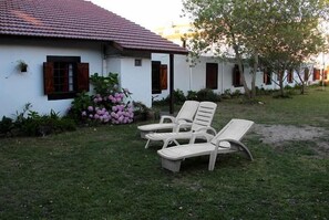 A white building with a tiled roof, a garden with pink flowers, and two white lounge chairs. - Hotel El Dorado (Mar de Ajo)