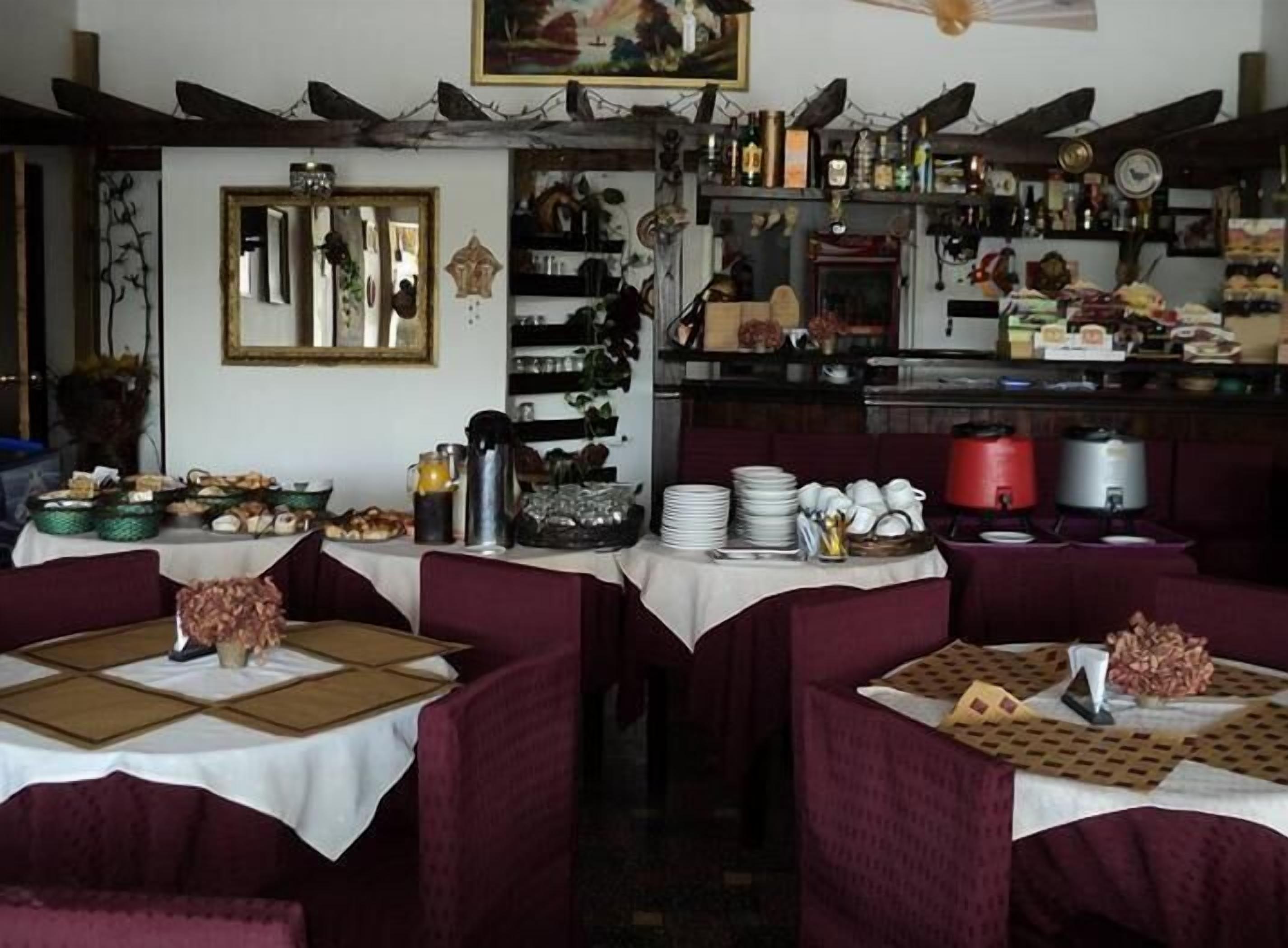 A restaurant with multiple tables covered with white tablecloths, red upholstered chairs, and a variety of dishes and condiments on the tables.