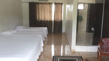 A hotel room with three single beds, a bathroom with a glass shower, and a wooden chair.