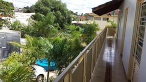En balkon med udsigt over en swimmingpool og grøn bevoksning.