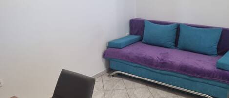 Una habitación con un sofá morado, una mesa de madera y piso de baldosas.