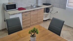 A compact kitchen with a microwave, sink, and wooden cabinets. There's a small potted plant on the dining table. - Apartments Marija Sukošan (Sukosan)