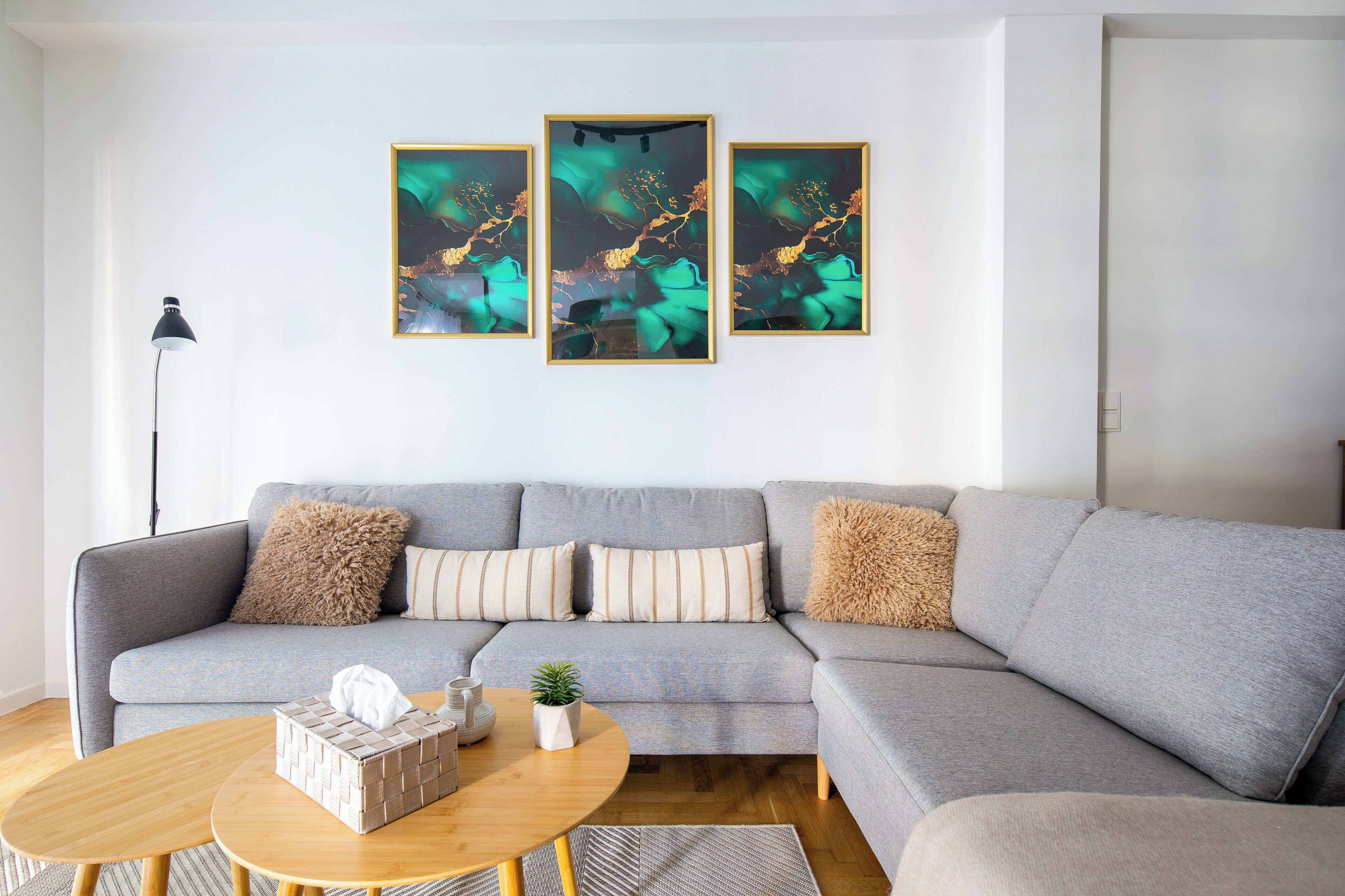 A modern living room with a grey sectional sofa, a round wooden coffee table, and three framed abstract paintings on the wall.