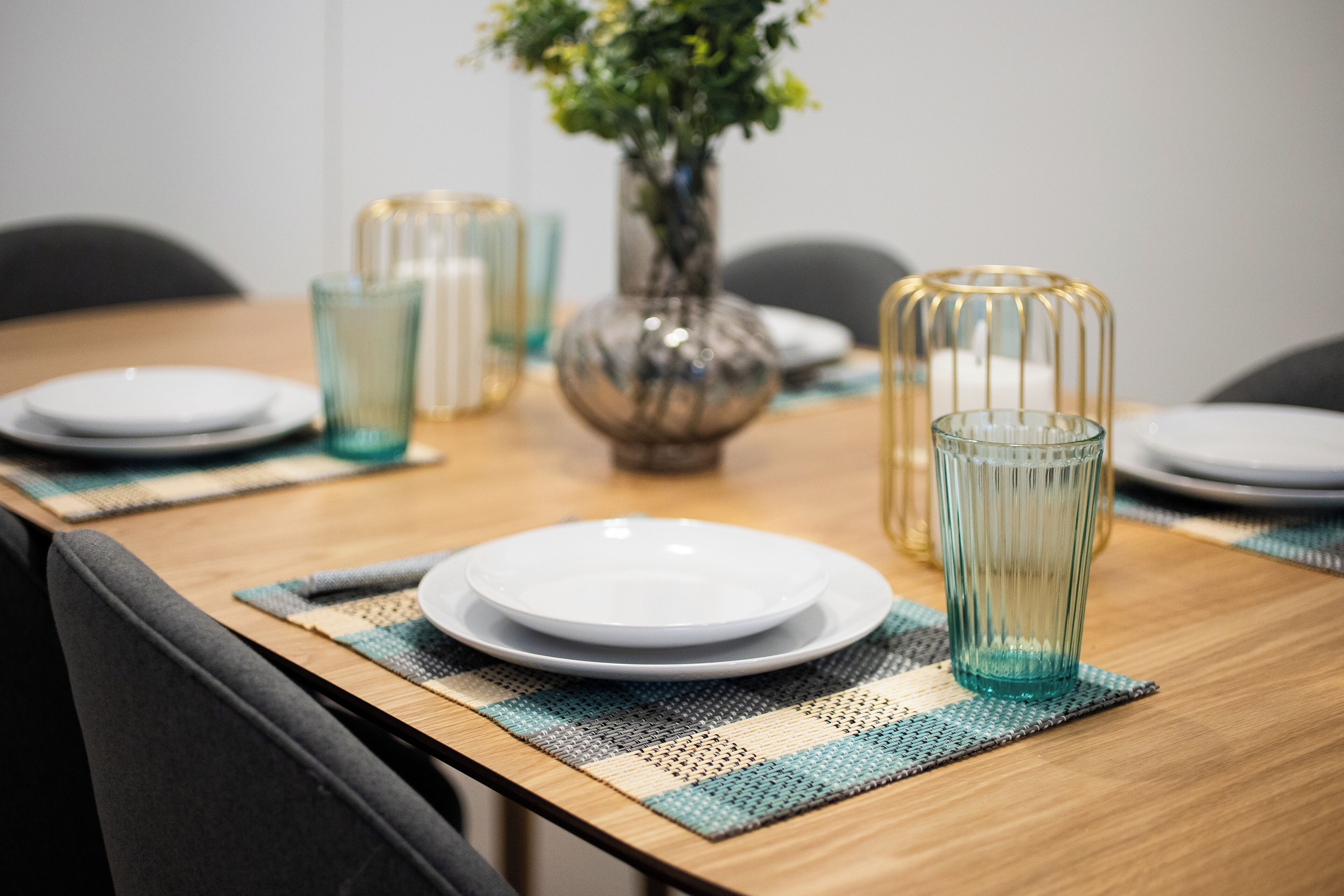 Una mesa de comedor con platos, vasos y un florero con flores.