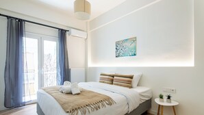 A modern bedroom with a large bed, a small bedside table with plants, and a window with curtains. - Mystique 2-Bedroom Apartment in Athens (Athens)