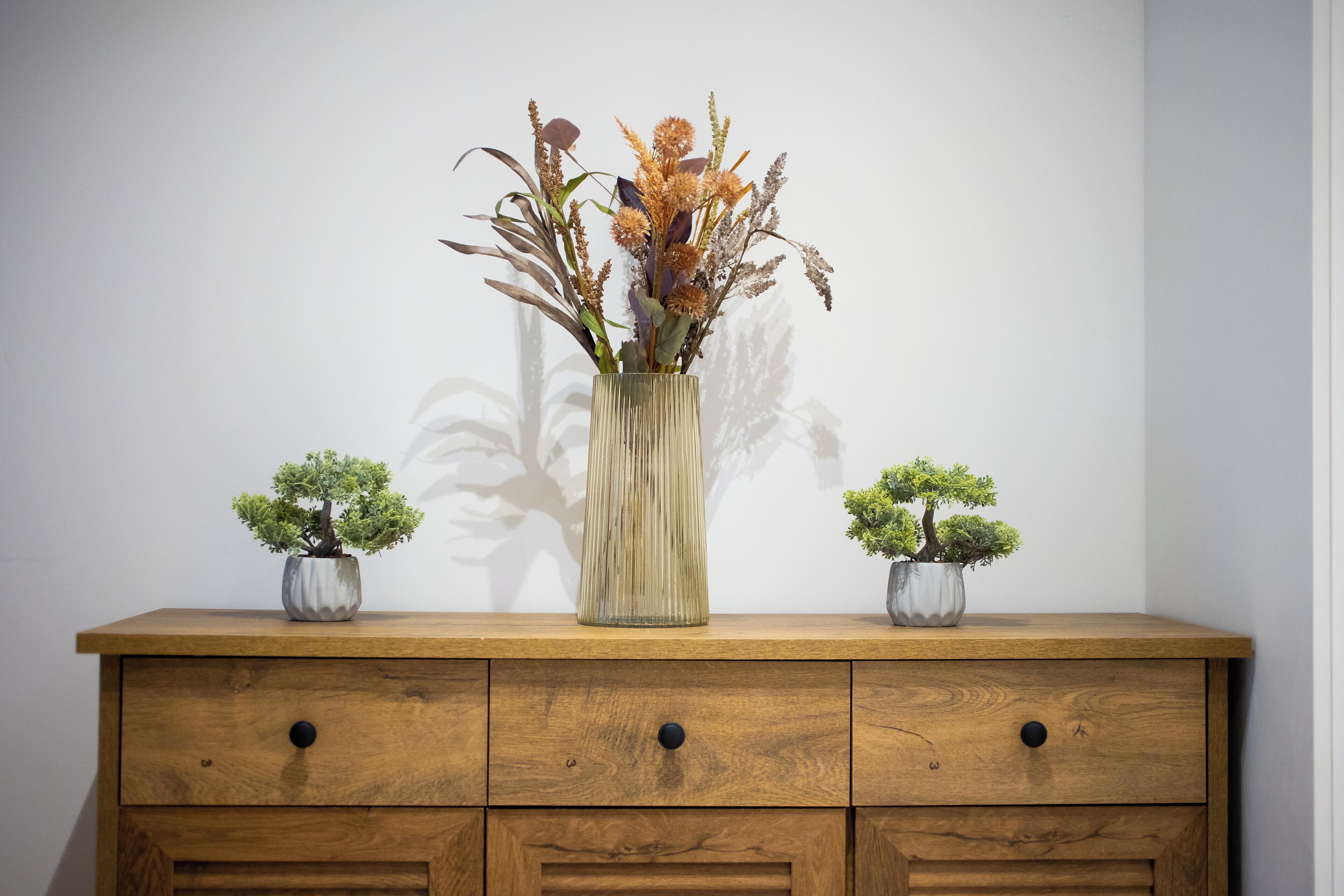 A wooden dresser with three potted plants, two on the sides and one in the center.
