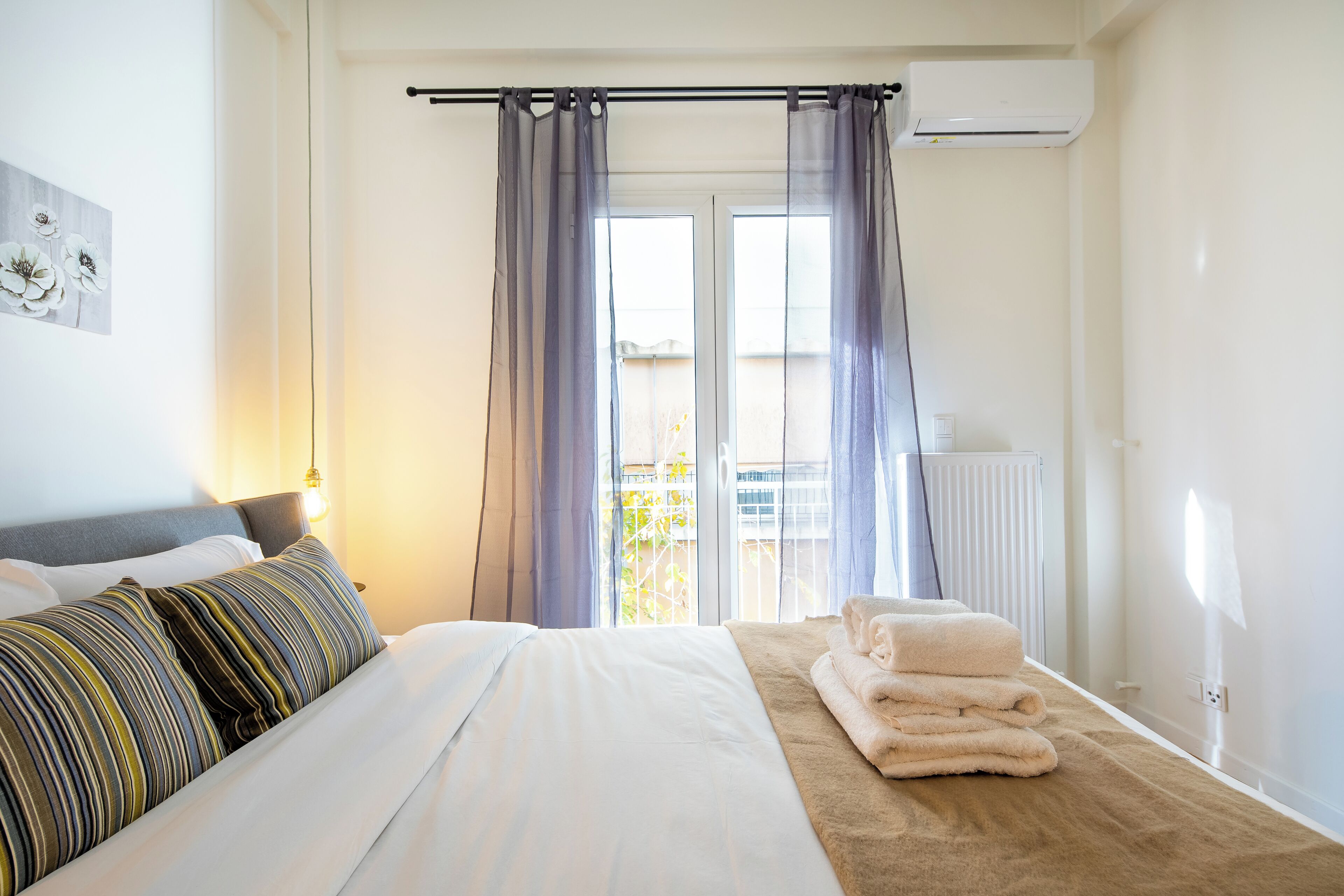 Et hotelværelse med en seng, et vindue med gardiner, en radiator og et håndklædestak.