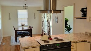 Una cocina con extractor de acero inoxidable, horno empotrado y comedor con mesa y sillas.