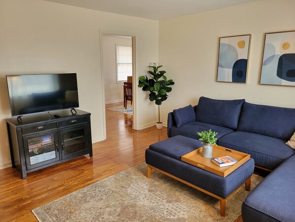 A living room with a TV, dark blue sofa, wooden coffee table, and a potted plant.