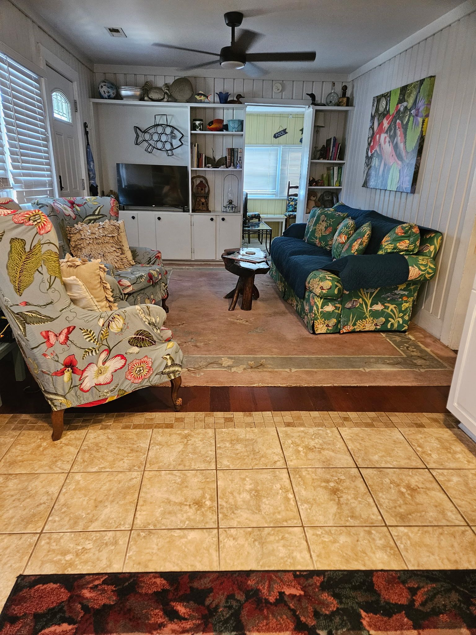 A living room with a sofa, armchair, and a coffee table. There is a television and a bookshelf in the background.