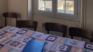 A room with a table covered by a patterned tablecloth, two chairs, and a window with lace curtains.