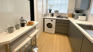 Una cuina moderna amb rentadora integrada, cafetera i finestra amb persianes.