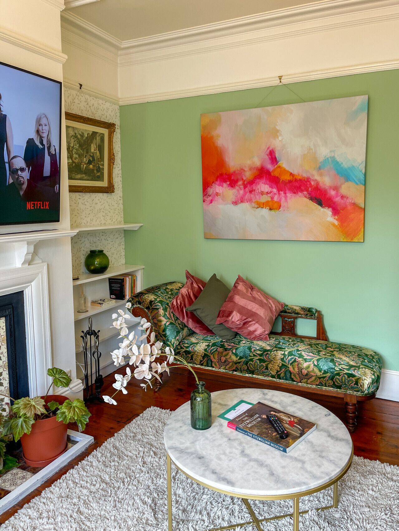 Een woonkamer met een bank, een salontafel, een open haard, een schilderij en een televisie waarop een Netflix-programma wordt vertoond.