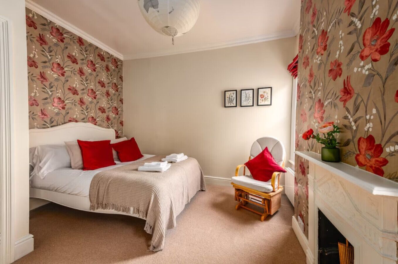 A bedroom with a bed, a chair, a fireplace, and floral wallpaper.