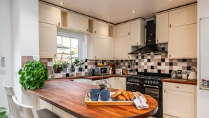 A modern kitchen with a wooden island, white cabinets, a black stove, and a window providing natural light. - Spacious Five Bed Home in the Heart of Cambridge (Cambridge)