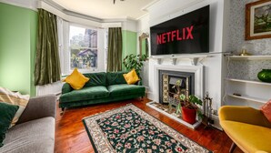 A living room with a green sofa, a fireplace, and a large TV screen displaying "NETFLIX". - Spacious Five Bed Home in the Heart of Cambridge (Cambridge)