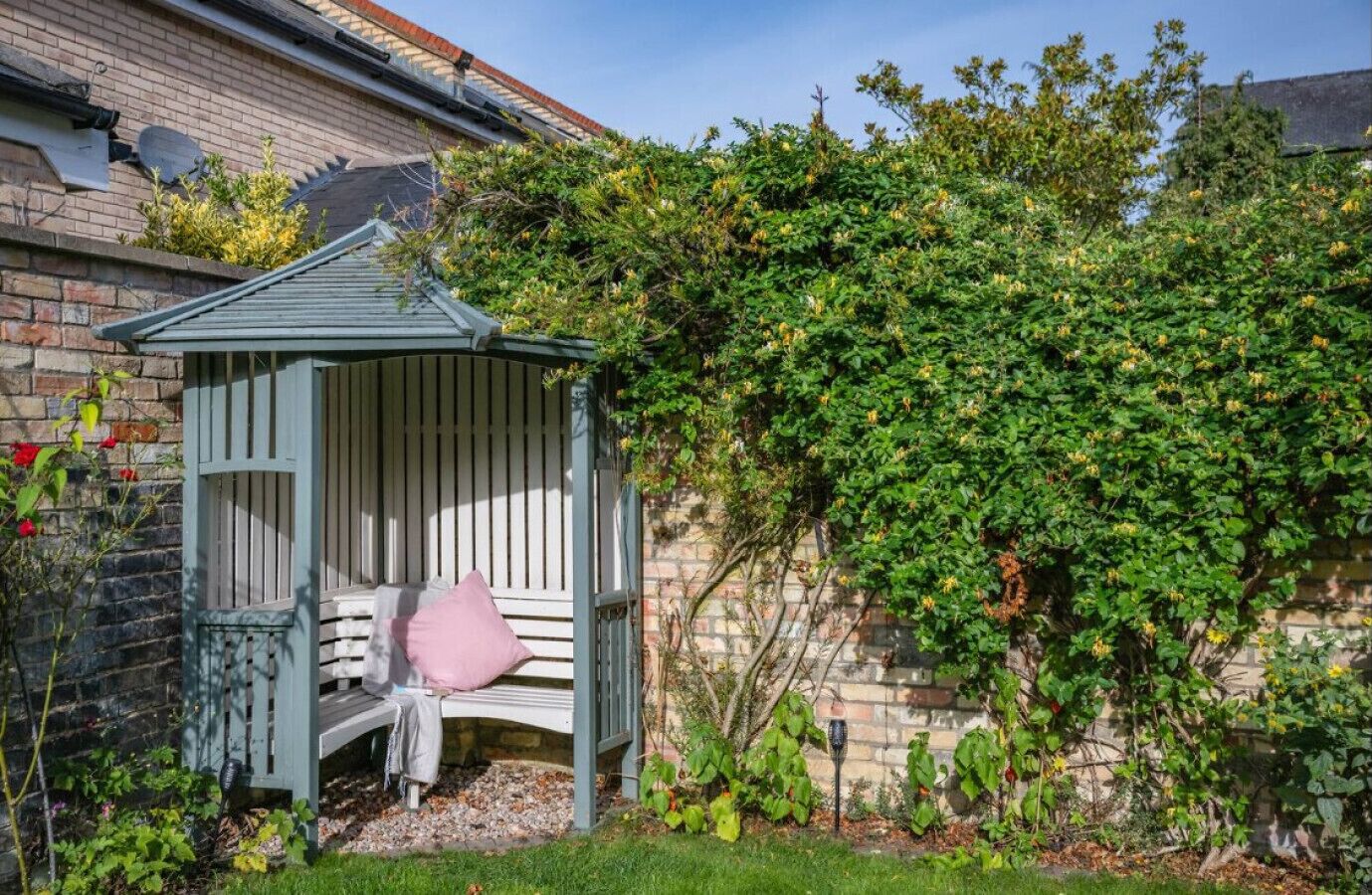 Un jardin avec un banc en bois, un mur en briques et une plante grimpante.