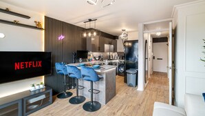 A modern kitchen with a central island, bar stools, and a built-in TV displaying 'NETFLIX'.