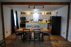 Een moderne keuken met witte kasten, een eettafel met stoelen en een zwarte koelkast.
