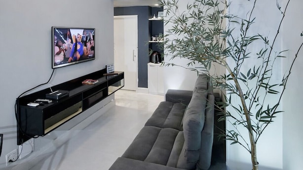 A modern living room with a grey sofa, a flat-screen TV, a black entertainment unit, and a bamboo plant. - PRIME location: Ipanema, Copacabana and Lagoa — all within reach (Lagoa Rio de Janeiro)