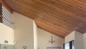A living room with a wooden ceiling, a leather sofa, a coffee table, a dining area with chairs, and a TV.