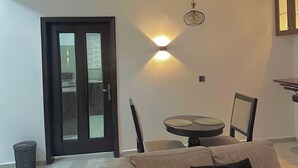 A living room with a sofa, a dining table with chairs, a ceiling light fixture, and a door with glass panels. - Charming 2-bedroom apartment with AC, WiFi in the Heart of Wuse II, Abuja. (Abuja)