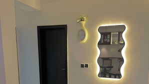 A hallway with a black door, a wall-mounted clock, and a decorative mirror with integrated lighting. - Charming 2-bedroom apartment with AC, WiFi in the Heart of Wuse II, Abuja. (Abuja)