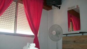 A bedroom with a bed, a fan, a mirror, and a window with curtains. - Hotel Gli Amici (Mar de Ajo)