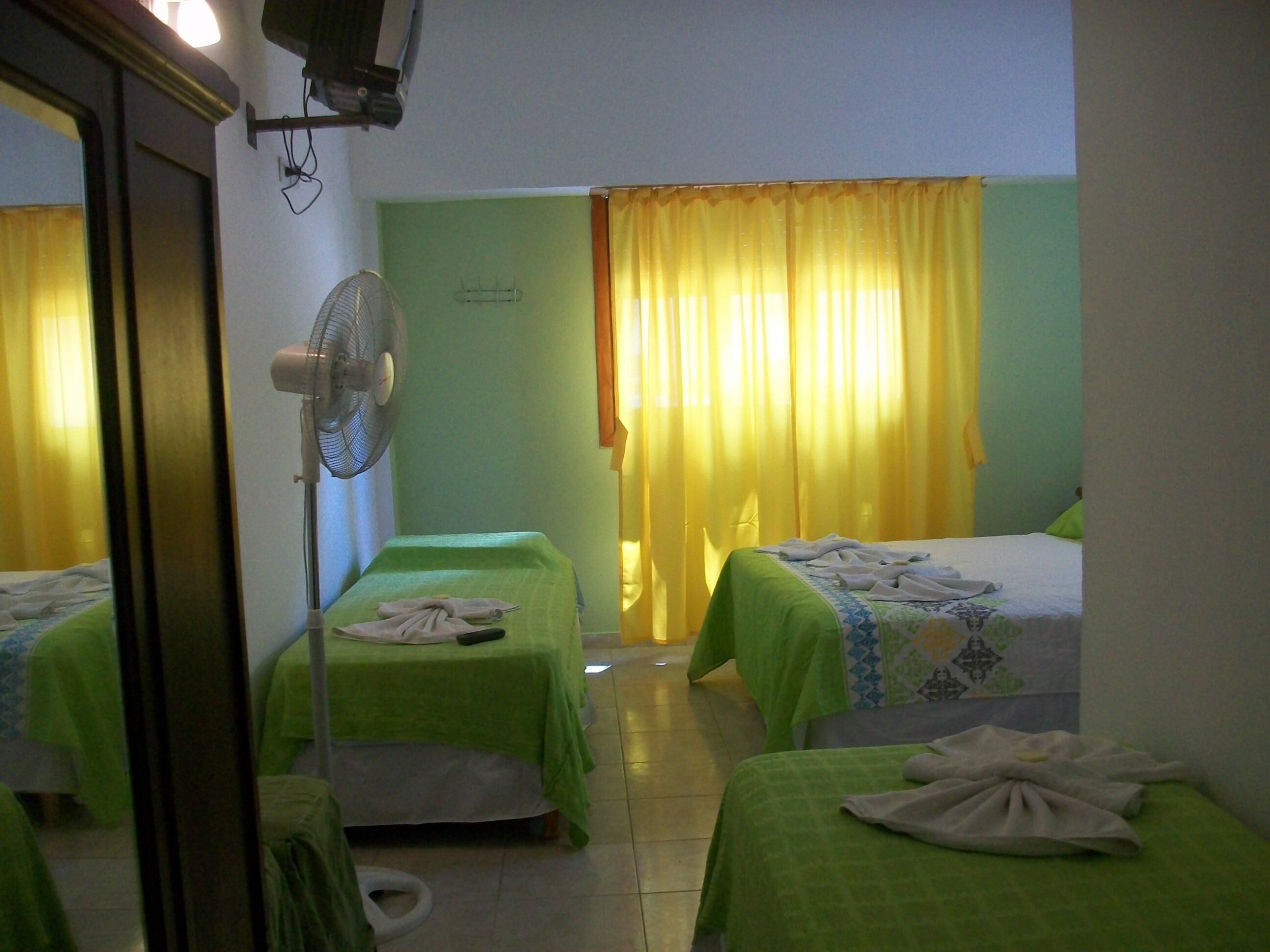 Una habitaci ón de hotel con dos camas individuales, un ventilador de pie y una cortina amarilla.