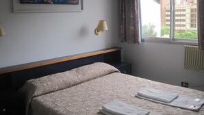 Een hotelkamer met een bed, een schilderij aan de muur, een raam met gordijnen en een lamp.