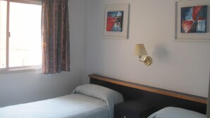 Een hotelkamer met twee bedden, een raam met gordijnen en twee abstracte schilderijen aan de muur.