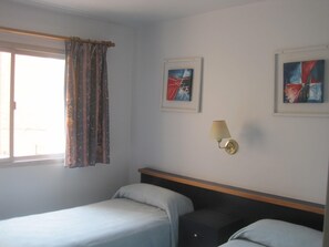 A hotel room with two beds, a window with curtains, and two abstract paintings on the wall.