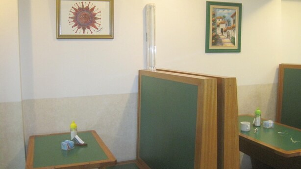 Een toiletruimte met houten scheidingswanden, een klein tafeltje met een fles en zakdoekjes, en twee ingelijste foto's aan de muur.