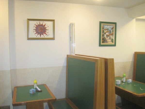 A restroom with wooden dividers, a small table with a bottle and tissues, and two framed pictures on the wall.