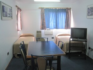 A small, simple room with two beds, a table, and a TV.