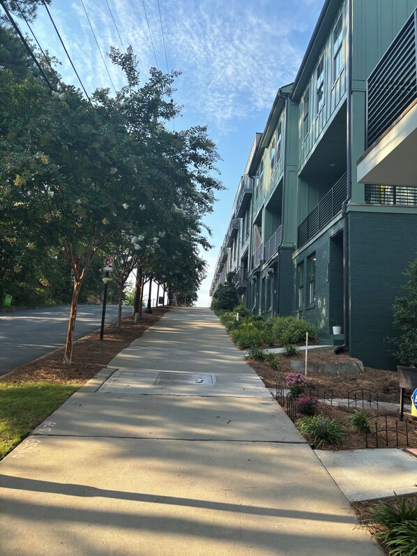 A residential street with a sidewalk, trees, and modern buildings with balconies.