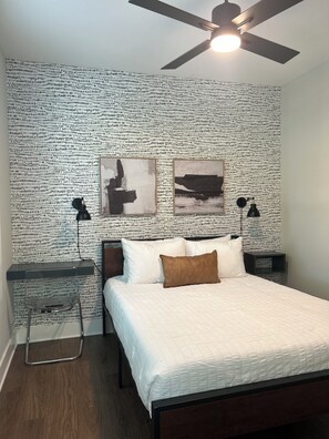 A bedroom with a patterned wall, a bed with white bedding, two bedside tables with lamps, and a ceiling fan.