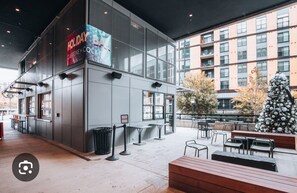 An outdoor seating area with tables and chairs, a Christmas tree, and a building with a 'Holiday Caffeine' sign.