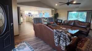 A spacious living room with a brown leather sofa, a coffee table, and a patterned rug. There is a kitchen in the background with bar stools and a dining area. - Rest your Kicks off of Route 66 at Rain Valley Inn (Flagstaff)