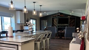 A modern kitchen with a central island, bar stools, pendant lighting, and a view into the living area. - Rest your Kicks off of Route 66 at Rain Valley Inn (Flagstaff)