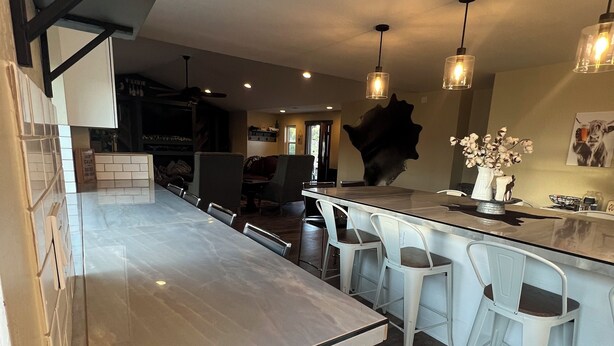 A modern kitchen with a central island, bar stools, pendant lighting, and a large decorative wall piece. - Rest your Kicks off of Route 66 at Rain Valley Inn (Flagstaff)