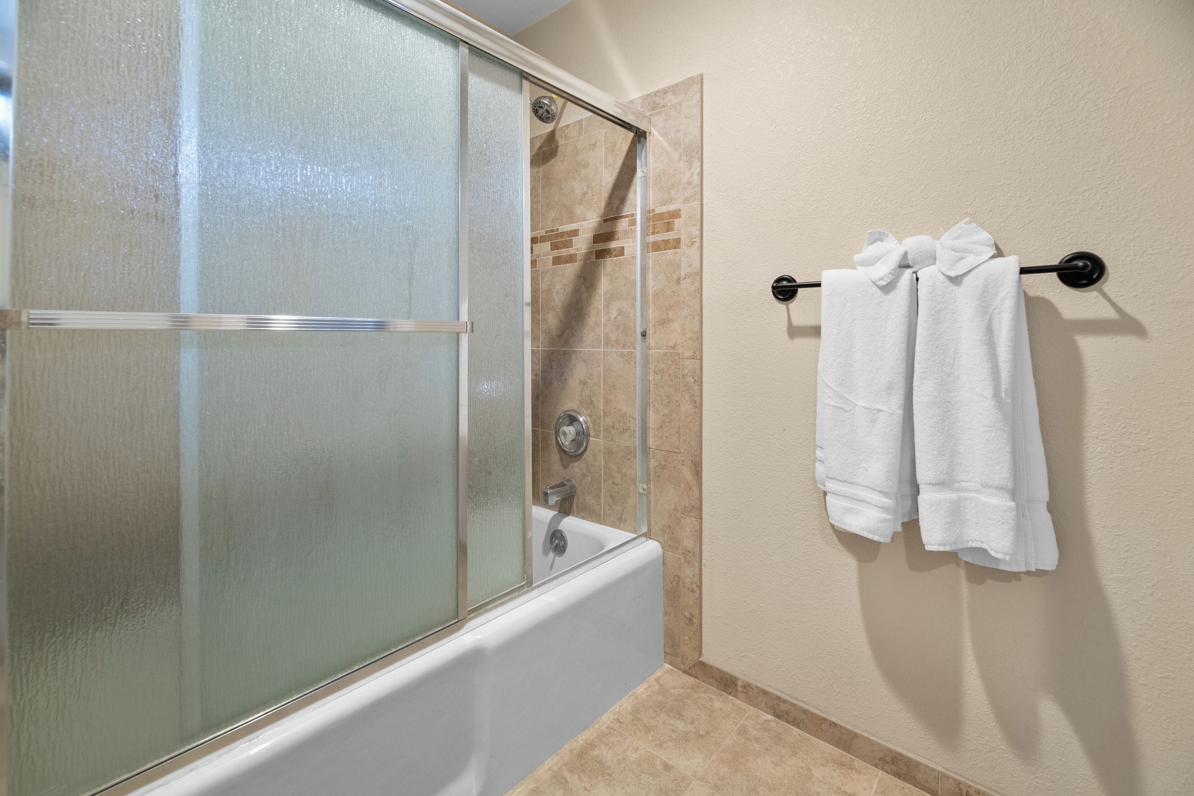 A bathroom with a glass-enclosed shower, a white bathtub, and two white towels hanging on a towel rack.