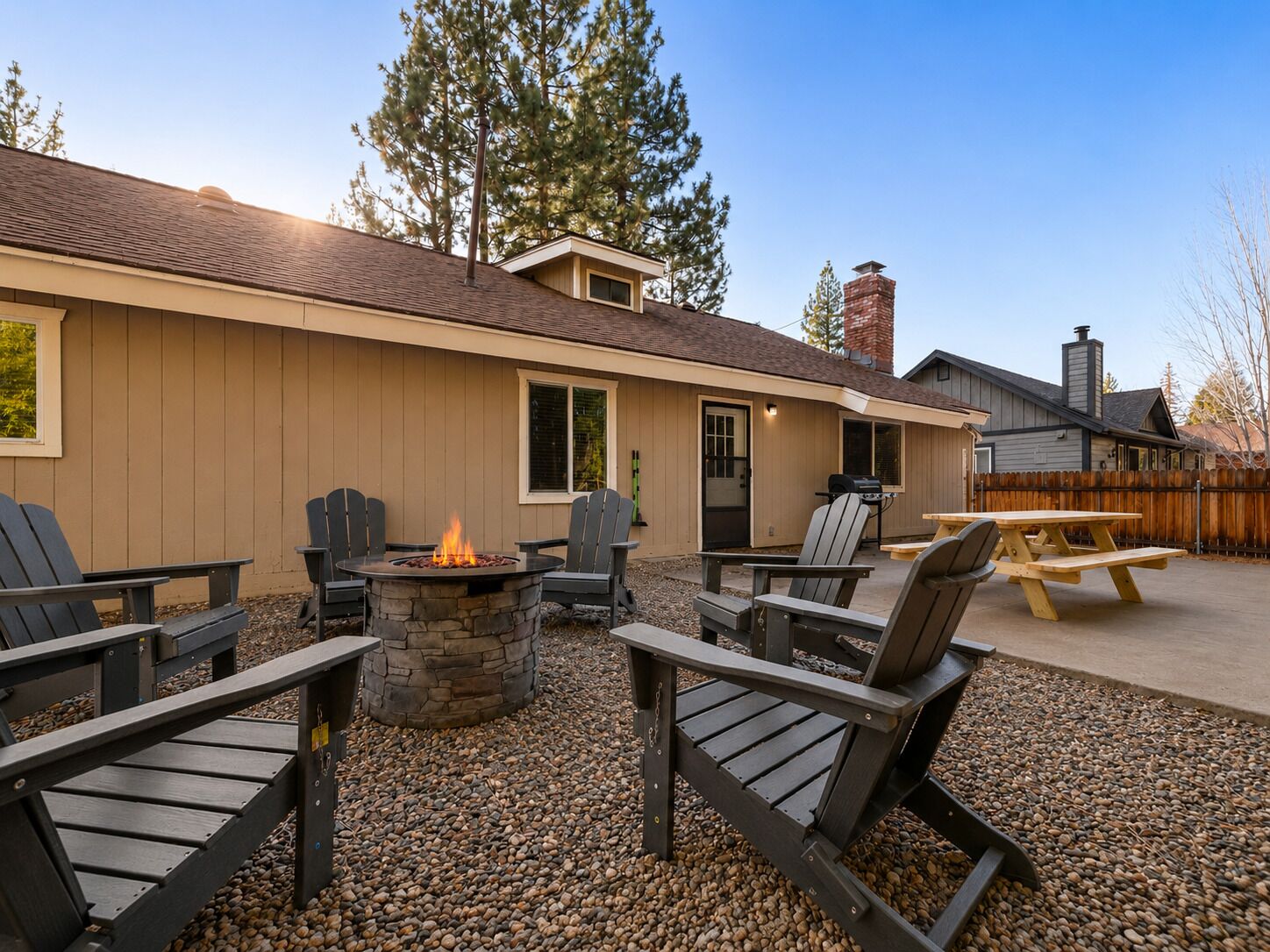 A patio area with Adirondack chairs, a stone fire pit, and a wooden table.